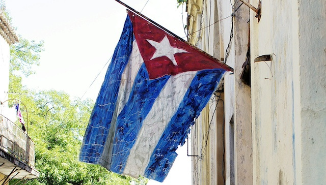 A cracked painted Cuban flag hanging from a building.