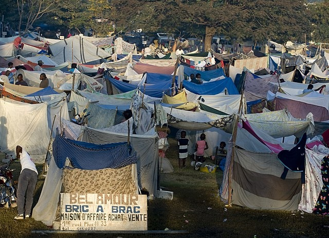 A field of makeshift tents with a sign that reads: "Bel Amour. Bric a brac. Maison d'affaire, achat, vente."