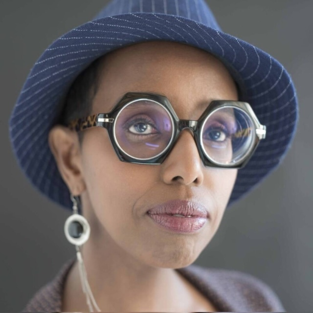 Close-up of Igiaba Scego in black hexagonal glasses and a blue striped fedora.