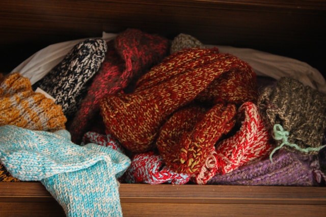 A tangle of multicolored knitted garments in a wooden drawer.