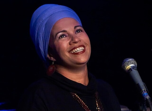 A singer in a blue turban and red lipstick in front of a microphone.