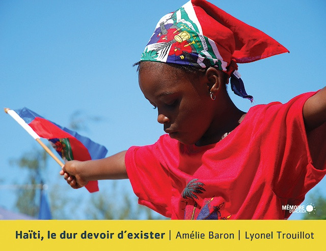 A young Haitian girl in a bandana and red t-shirt holds a Haitian flag, her arms outstretched.