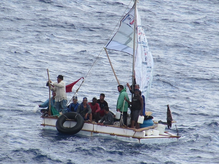 Ten men riding a small homemade sailboat in the middle of the ocean.