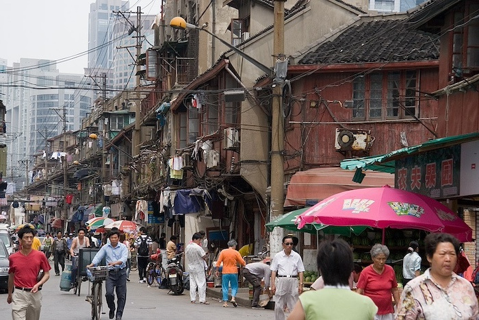 People walk and bike down a pedestrian street. Shops line the street, with apartments above them.