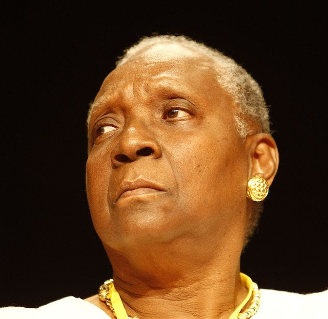 Close up portrait of author Maryse Condé, looking partly sideways, and wearing golden earrings and necklace.