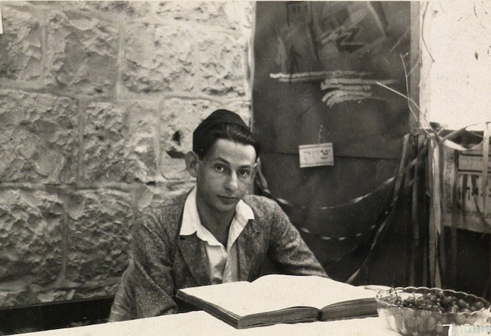 A young man in a yarmulke sits in front of an open book.