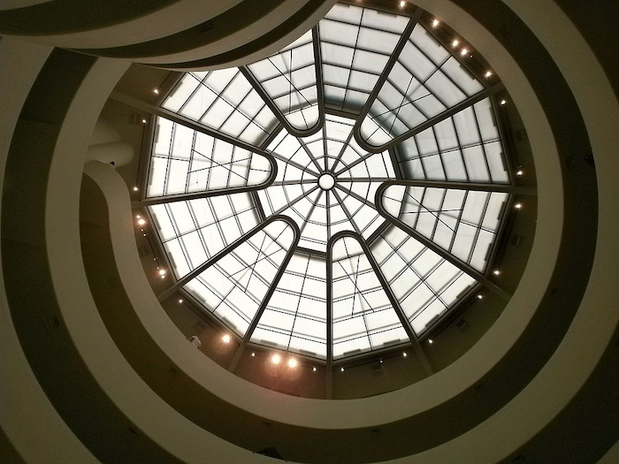 A view from below of the Guggenheim's spiraling white ramps, leading up to a round glass skylight.