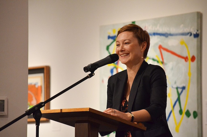 A woman in a black blazer stands behind a podium and microphone.