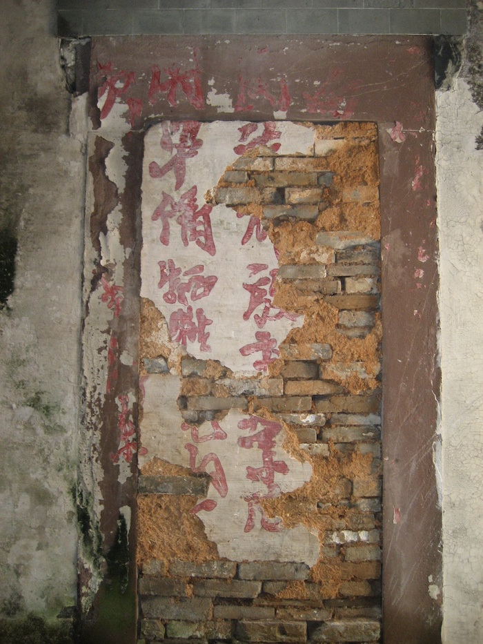 Faded red Chinese characters painted on a brick wall.