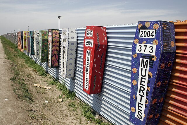 An image of painted coffins affixed on a tin wall, with the year and number of deaths each year prominently written on them.