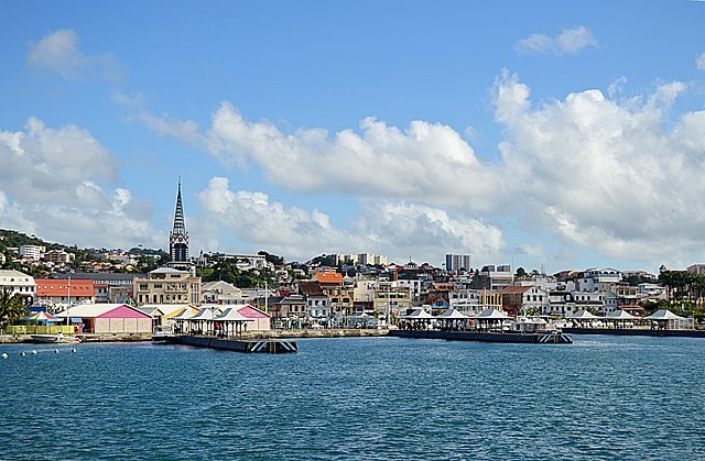 An image of a harbor on a mostly sunny day, with docks and a bustling city visible across the blue waters.