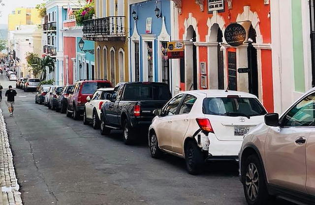 Image of several cars parallel parked along a street with colourful, arched doorways.