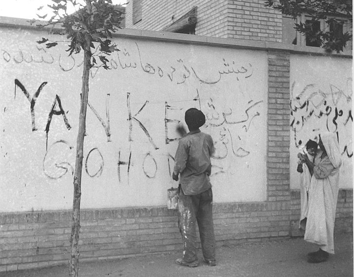 A resident of Tehran washes "Yankee Go Home" graffiti from a wall in the capital city of Iran, Aug. 21, 1953. AP, Public domain.