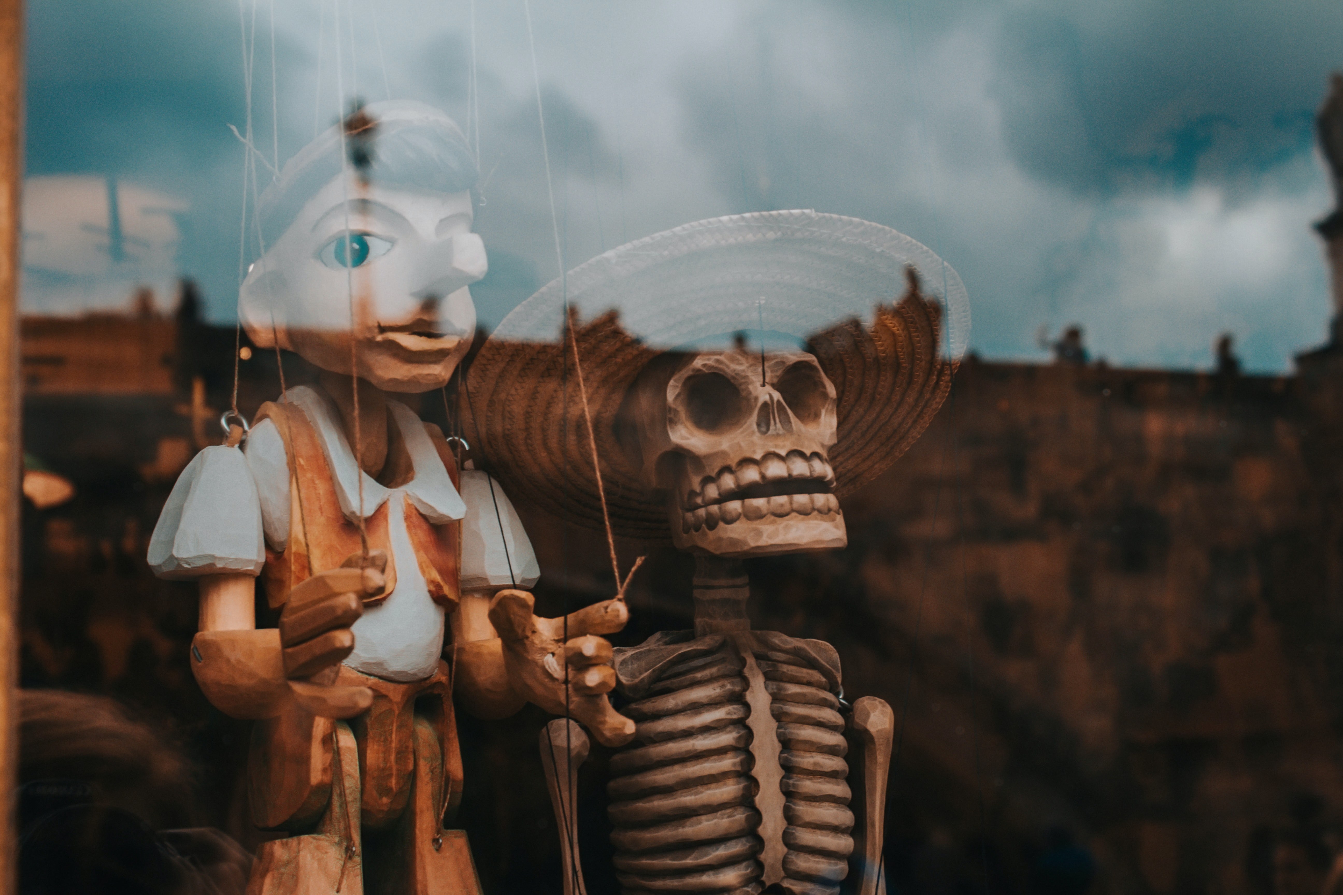 A Pinocchio marionette and a skeleton marionette behind a glass shop window.